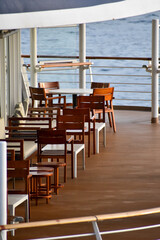 Outdoor seats on passenger ship deck with the calm seascape. Cruise ship deck. Wooden promenade deck on a luxury cruise liner. Ocean in background.