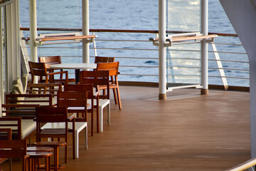 Outdoor seats on passenger ship deck with the calm seascape. Cruise ship deck. Wooden promenade deck on a luxury cruise liner. Ocean in background.