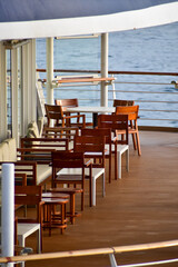 Outdoor seats on passenger ship deck with the calm seascape. Cruise ship deck. Wooden promenade deck on a luxury cruise liner. Ocean in background.