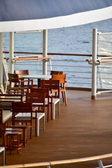 Outdoor seats on passenger ship deck with the calm seascape. Cruise ship deck. Wooden promenade deck on a luxury cruise liner. Ocean in background.