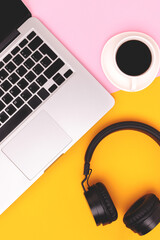 Headphones, cup of black coffee and laptop on a pink and yellow background. Distance education concept.