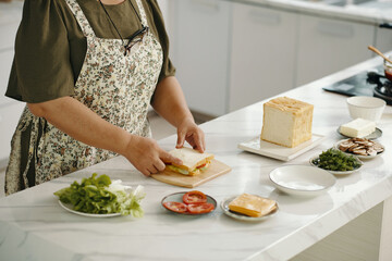 Close-up of senior woman preparing sandwich for breakfast in the kitchen