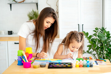 mom and a drawing teacher teaches a little girl child to draw with paints and colored pencils, fun drawing lessons at an art school