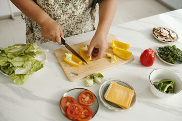Close-up of housewife preparing salad from fresh vegetables at table in the kitchen