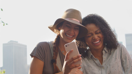 Two Female Friends Looking At Photos On Phone And Laughing By Manhattan Skyline