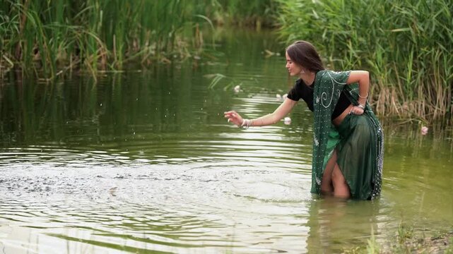 Beautiful  brunette extra long braided hair girl in Indian traditional dress posing near river . Portrait of young attractive stylish woman in sari on  green nature background.