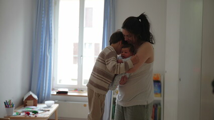 Mother holding newborn while embracing her older child, capturing a tender family moment filled with love and affection in a bright and cozy room