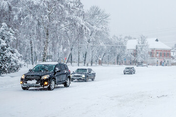 Cars driving on a slippery snowy road on a city street during a heavy snowfall in the evening in winter. Traffic disruption due to blizzards and blizzards. Weather forecast