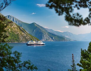 A ship majestically floats in the sea between mountains, with summer sunlight and framed leaves.