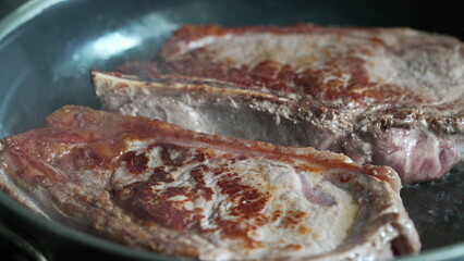 Partially cooked steaks in a pan, starting to brown, close-up view, home cooking, delicious meal in progress, fresh beef, culinary preparation, sizzling sound, detailed kitchen scene