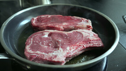 Raw steaks sizzling in a hot pan, lightly salted, beginning to cook, close-up view of fresh beef, home cooking process, preparing a delicious meal, culinary detail, kitchen scene