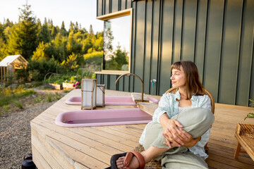 A woman relaxes on a wooden deck with a peaceful mountain view, surrounded by nature. The calm...