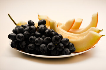Pieces of melon and grapes on a white plate. Juicy fruits.