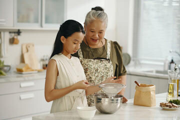 Girl learning to bake cake together with her grandma in the kitchen