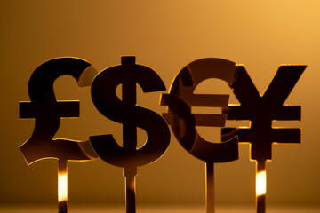 Close-up of four different currency symbols: the U.S. dollar, the British pound, the Euro,and the Japanese yen, on sticks in front of a gold background © JUN LI