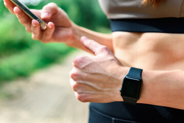 Young woman with fitness bracelet tracking cardio workout results after running outdoor.