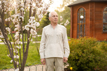 Senior Ukrainian man outside on sunny day near blooming tree wearing Ukrainian embroidered shirt