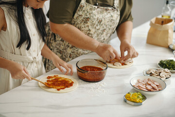 Family cooking together homemade pizza at table in the kitchen