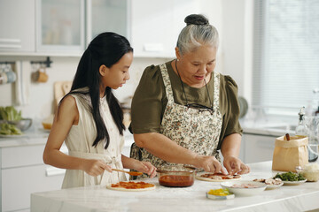Grandma and granddaughter spending time in the kitchen, they cooking homemade pizza together