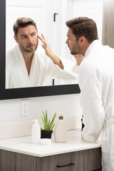 A man is applying lotion to his face in front of a mirror. Concept of self-care and personal...