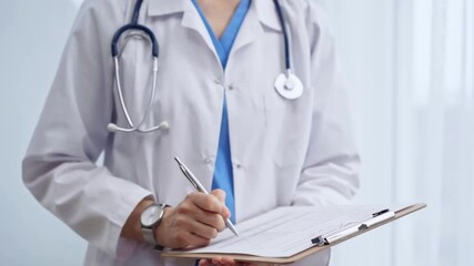 Female doctor taking notes on clipboard. Close-up of a unrecognizable female healthcare professional writing and filling um medication history records form while standing straight in clinic