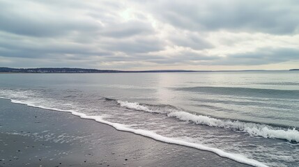 A cloudy grey sky over a calm sea, with waves gently lapping at the shore