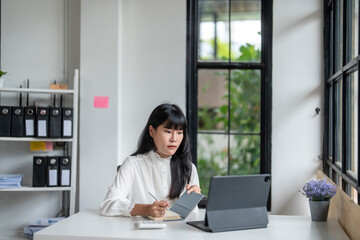 Fototapeta premium Asian businesswoman taking notes while having video call on tablet in office