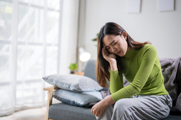 Obraz premium Young asian woman suffering from a headache at home on the sofa