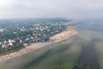 Fototapeta premium Aerial drone image of traditional numbered wicker, reed beach hut, or chair on the sand beach at the coastline of Laboe, the Baltic Sea in summer Germany with wooden walkway or path on cloudy day