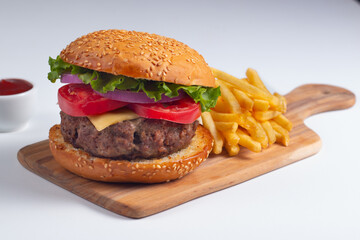 Homemade delicious hamburger with beef, onion, tomato, lettuce and cheese. Fresh burger close up on wooden rustic table with potato fries. Cheeseburger. Burger.