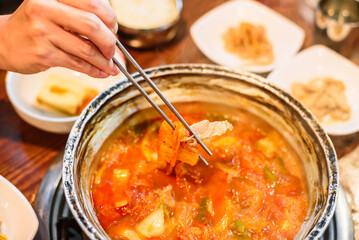 Chopsticks Picking Up Both Kimchi and Pork from Kimchi Stew in a Metal Pot