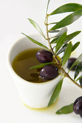 Extra Virgin Olive Oil in a White Plate and a Branch of Olives with Leaves on a White Background with Drops of Olive Oil.