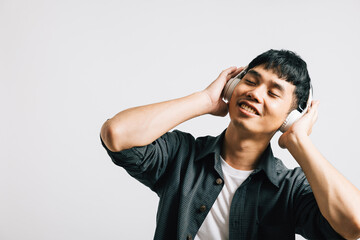 Portrait of a joyful young man, holding his phone and wearing Bluetooth headphones, immersed in the joy of listening to music. Studio shot isolated on white, showcasing his love for modern technology.