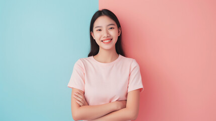 Obraz premium A young Asian woman with long black hair smiles confidently with folded arms against a split pastel pink and blue background, filled with joy.