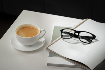 A Cup of Coffee, Glasses, and a Stack of Magazines on a White Tabletop