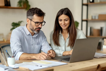 Fototapeta premium Two busy colleagues working together talking using laptop in office.