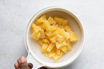 Overhead view of canned pineapple chunks being drained in white sieve, top view of pineapple pieces in a sieve