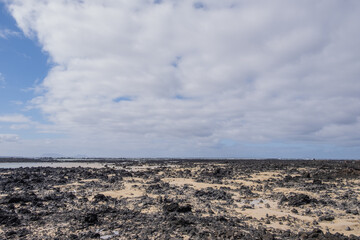 White sand beach with black rocks of volcanic origin. Mountains in the background and sky with big white clouds. Caletón Blanco, Lanzarote, Canary Islands, Spain