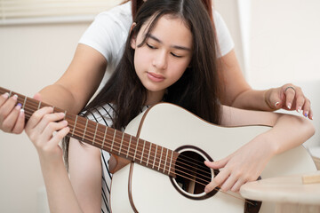 Fototapeta premium Teenager woman playing guitar with mother teaching at home 