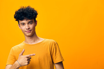 Young man pointing to the side on a vibrant orange background, showcasing a cheerful expression and casual attire, perfect for advertising and social media contexts