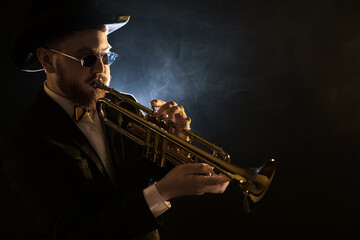 Professional musician playing trumpet on black background in smoke