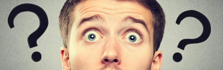 Naklejka premium Young man displays shock and confusion, eyes wide, mouth open, with question marks around him