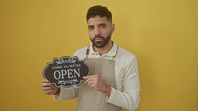 Confident young hispanic man in apron, singing while pensively thinking with a sober expression, standing alone over an isolated yellow background