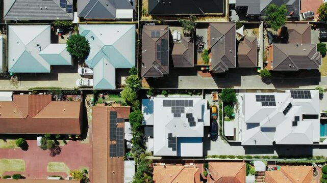 The rooftops of several homes showcase solar panels, surrounded by neatly arranged gardens and driveways under clear skies.