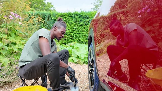 Hampshire England UK. 08.08.2024. Video.  Vateting a luxury red car man sitting on stool cleaning the alloy wheels and tyre.