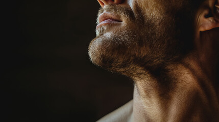Obraz premium Close-up of a man's bearded neck and chin, with subtle lighting enhancing the texture and contours of his skin and hair.
