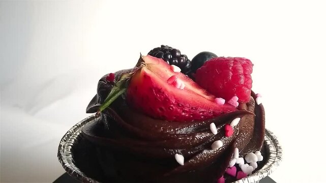 Chocolate mud cake with heartshaped sprinkles, strawberry, raspberry and blackberry topping in foil cupcake liner rotating.