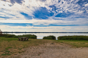Obraz premium Idyllischer Blick über den Raßnitzer See mit Picknickbank am Ufer, blauer Himmel mit Federwolken, ehemaliger Braunkohletagebau Merseburg-Ost, Schkopau, Saalekreis, Sachsen-Anhalt, Deutschland