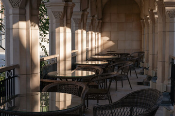 Tables, Chairs, Courtyard - Outdoor Seating Area With Sunlight Streaming Through Columns In A Historic Building. .