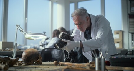 Senior archaeologist takes photo of fossil remains of prehistoric human skull and bones with camera...